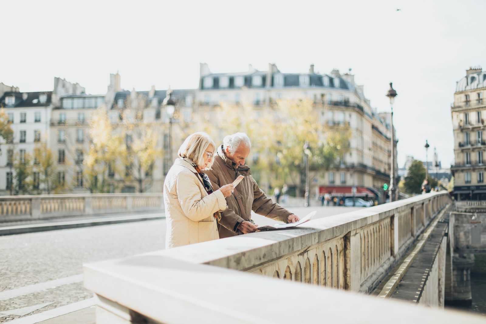 Older couple reading a map at a stone balustrade beside a river in a European city